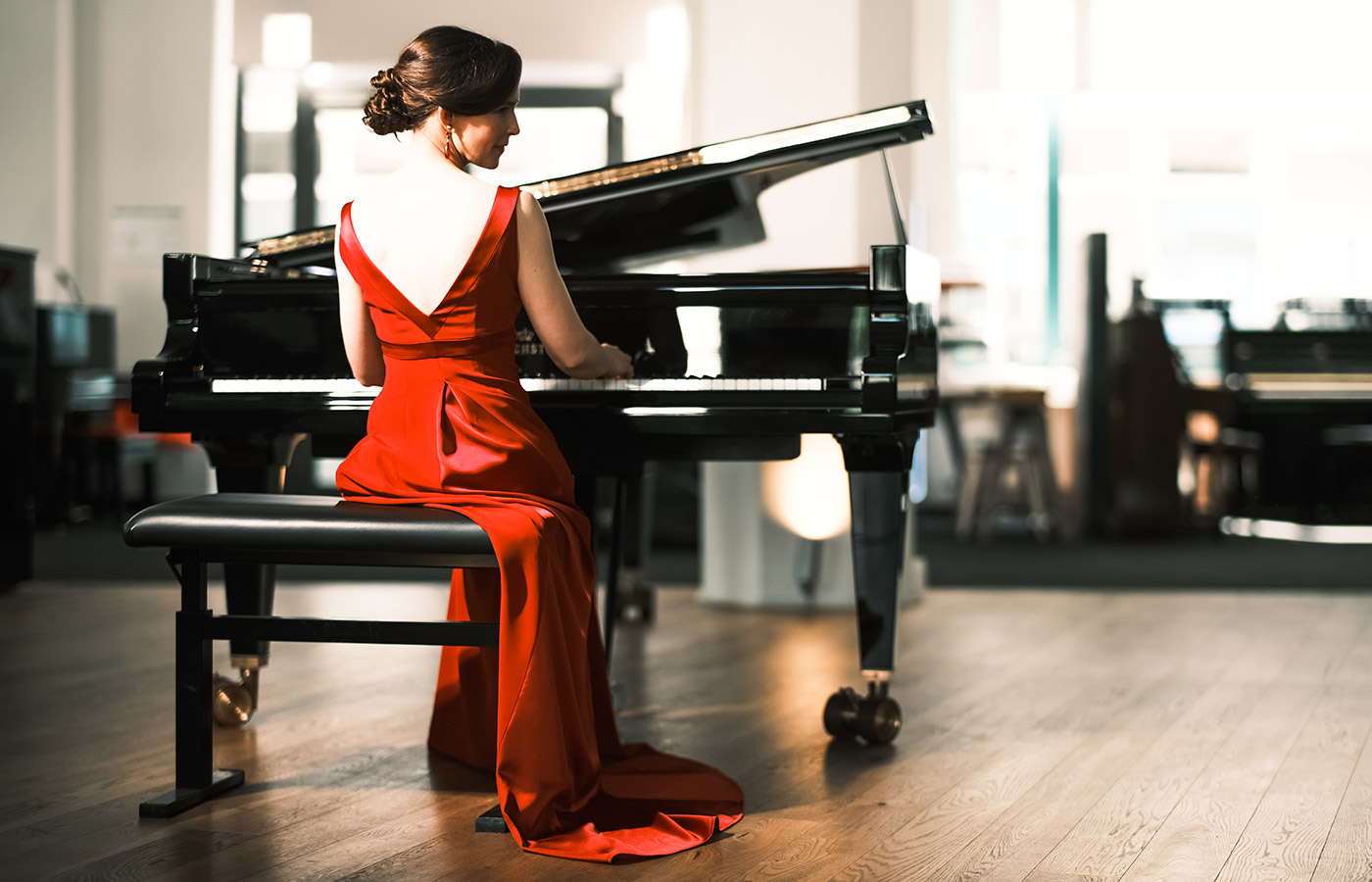 Pianistin Sophie Weidemann in einem roten Konzertkleid von Marillon Couture, Rückansicht am Flügel